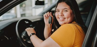 A woman sitting in a new car, holding the keys up.