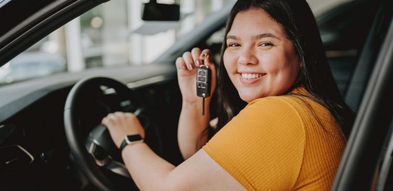 A woman sitting in a new car, holding the keys up.